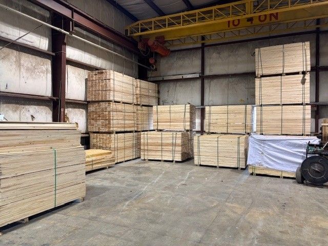 Stacked lumber and plywood sheets stored inside an industrial warehouse.