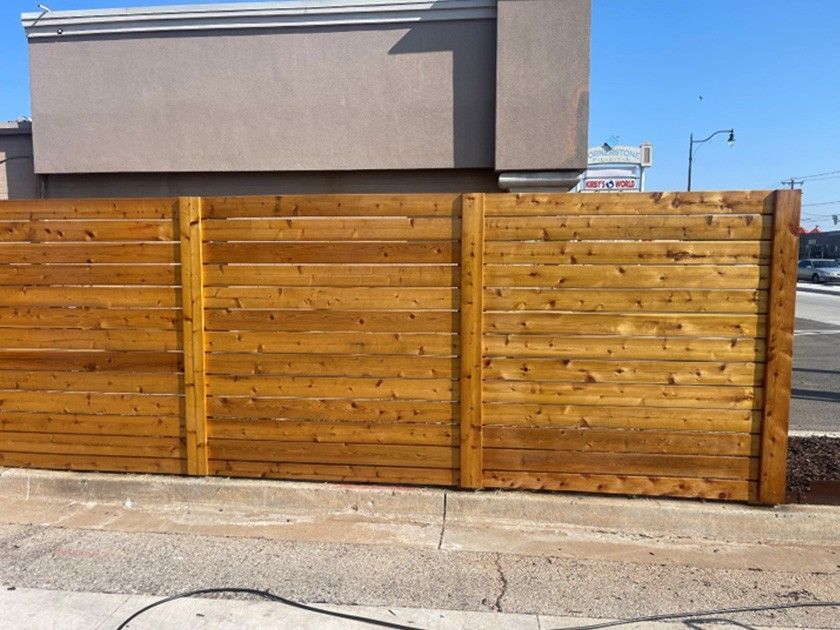 Wooden fence along a sidewalk in front of a building on a sunny day. Wooden fence along a sidewalk in front of a building on a sunny day.