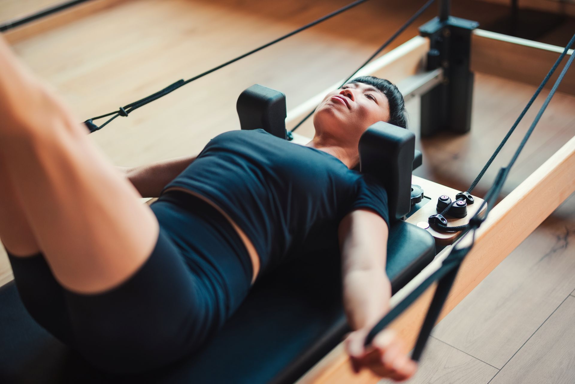 Person exercising on a Pilates reformer, lying back and pulling straps in a studio near Prelude at Medley.