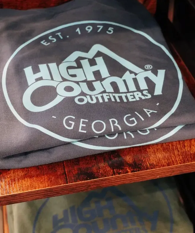 Dark shirt with white “High Country Outfitters Georgia” logo on a wooden surface near Prelude at Medley.