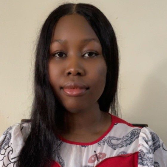 A person with long, straight dark hair wearing a white blouse with a red collar and a patterned design.