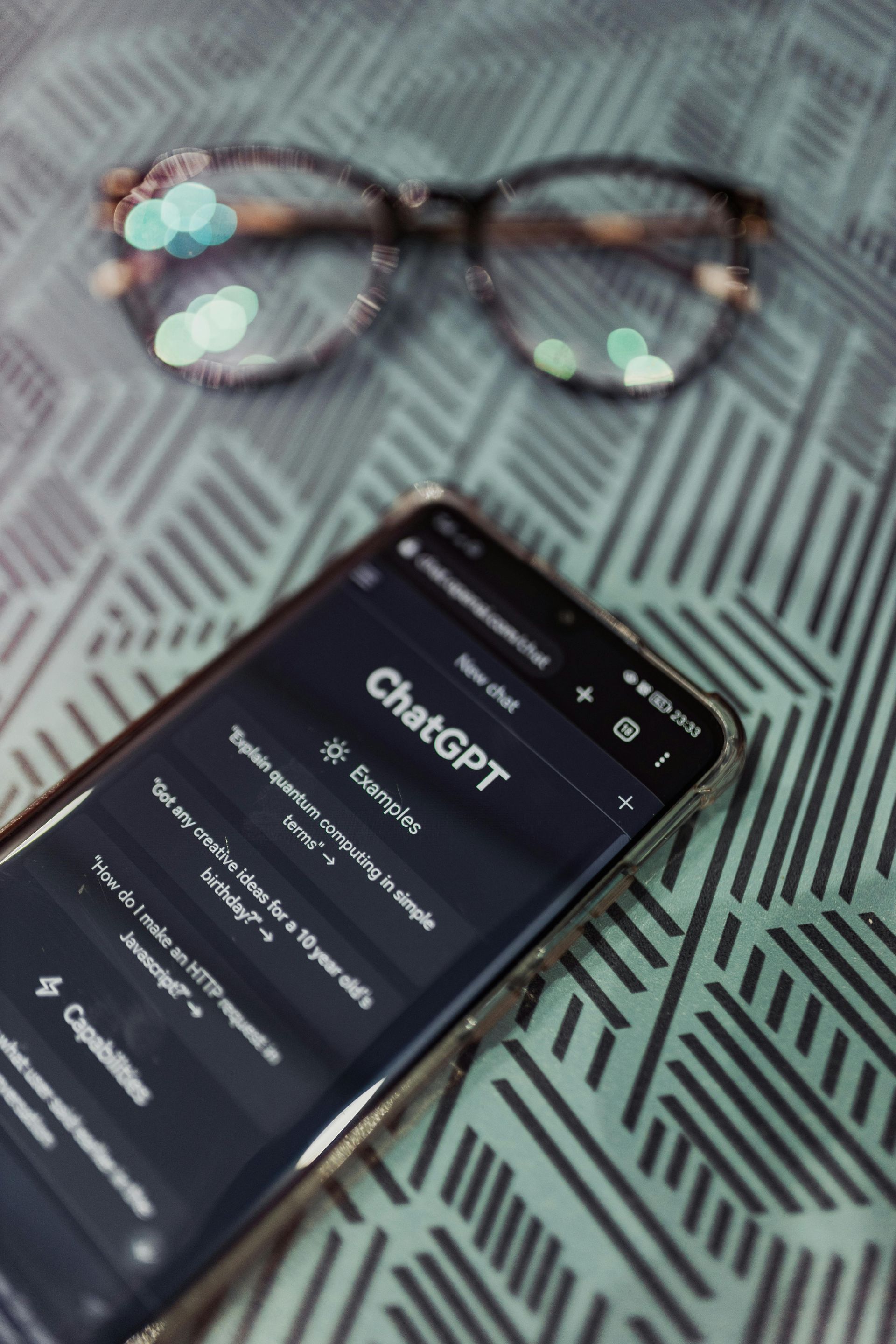 Smartphone displaying ChatGPT, with eyeglasses resting on a patterned surface.