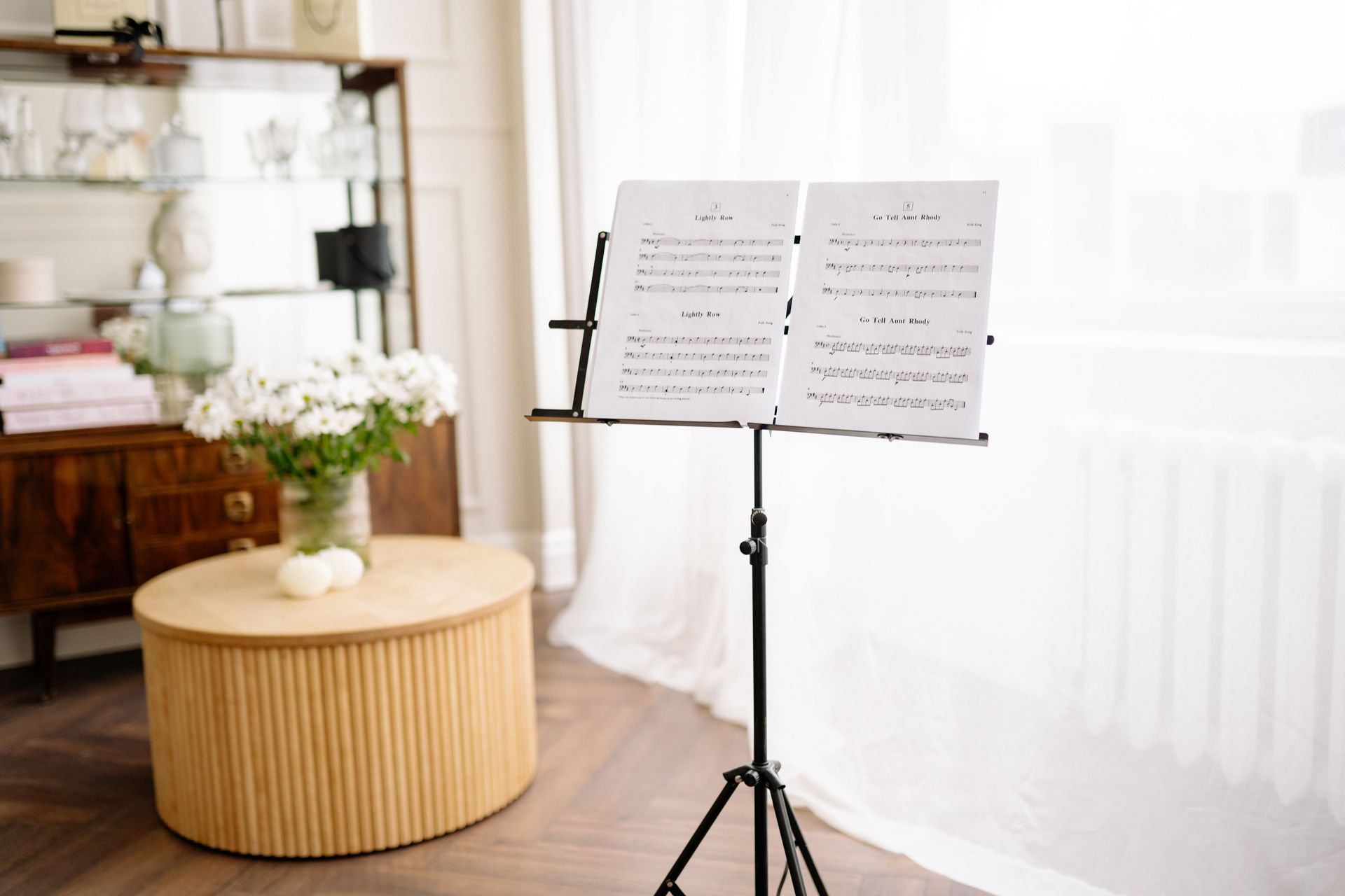 Music stand with sheet music in a bright living room beside a round table with flowers.
