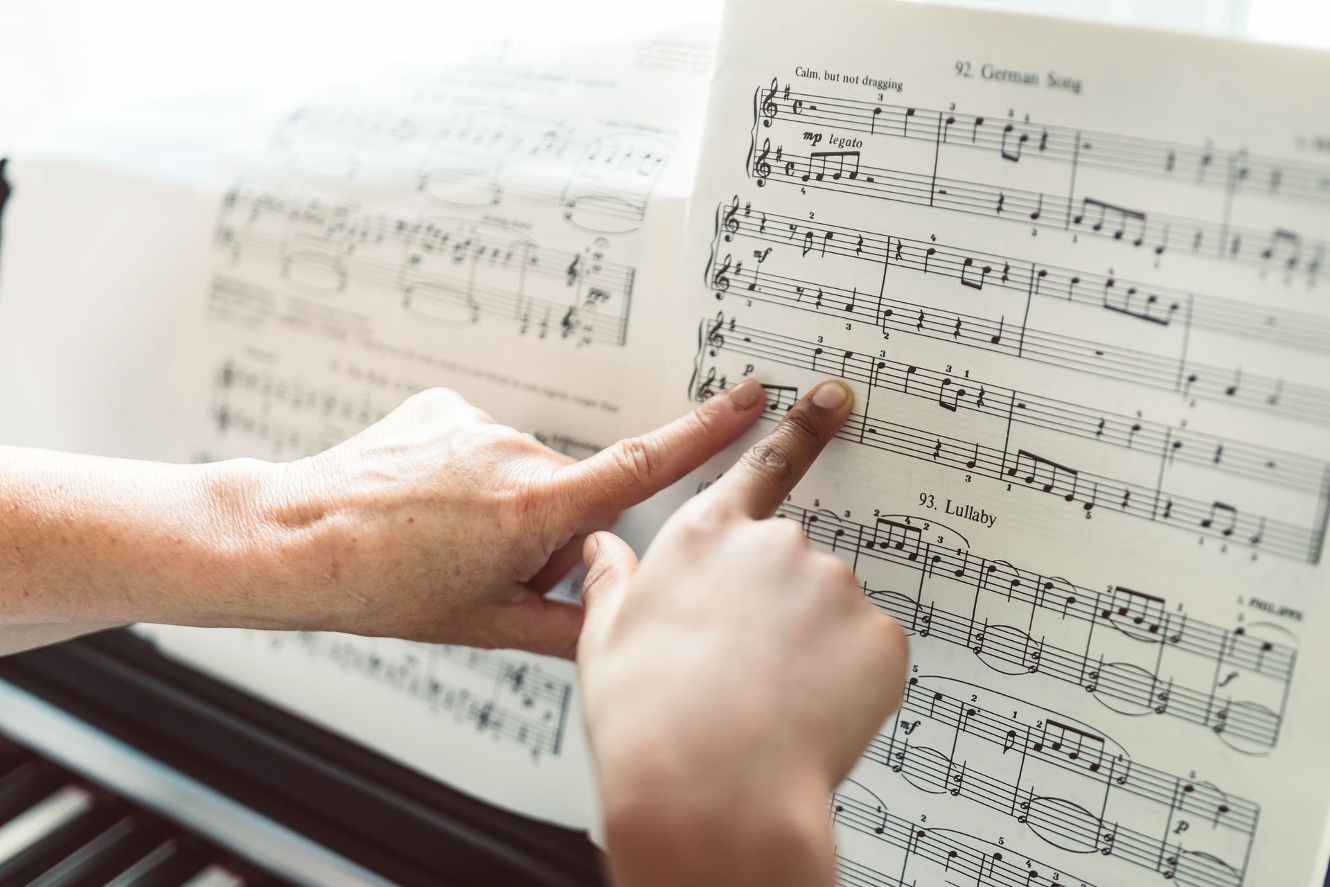 Hands pointing to sheet music in a book, following notes on a music stand.