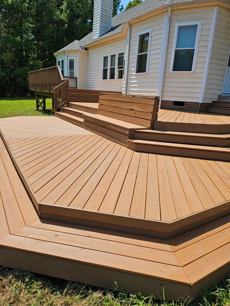 Wooden multi-level deck with stairs attached to a white house in a sunny backyard