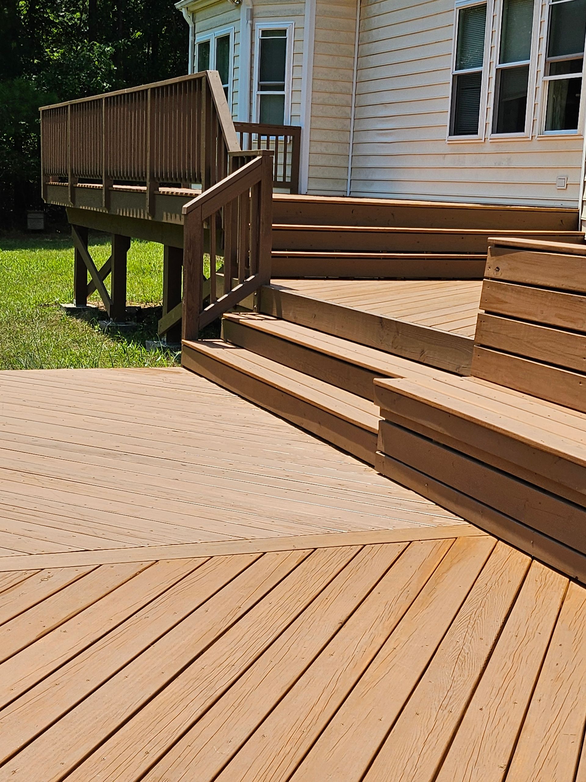 Wooden ramp and deck beside a house with tan siding and windows, in bright sunlight