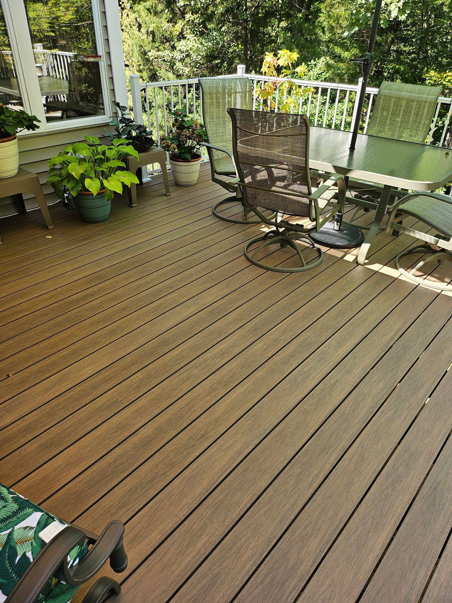 Wooden backyard deck with patio chairs, potted plants, and railing in sunlight