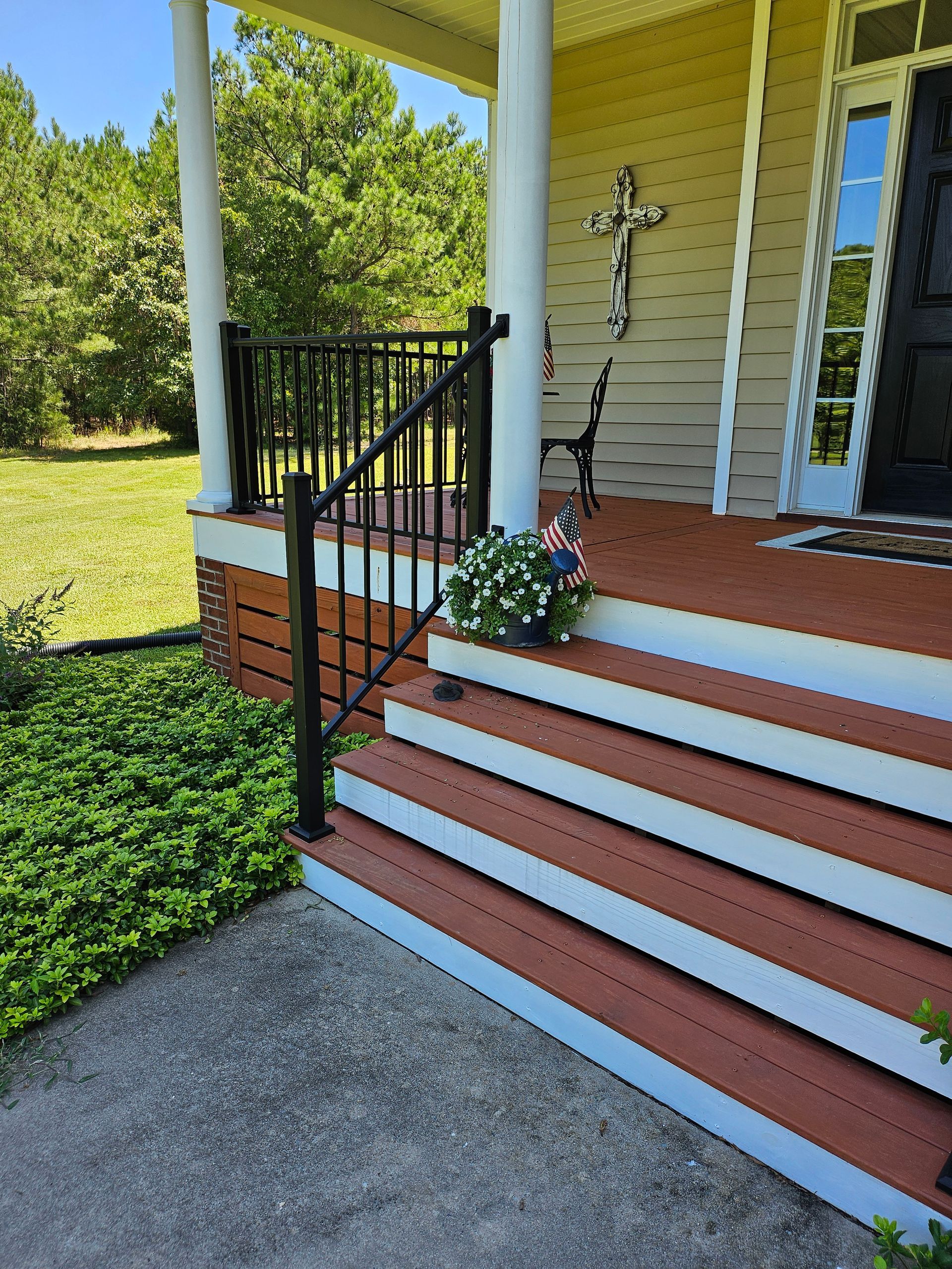 Front porch with red-and-white steps, black railing, white columns, and a potted flower arrangement.