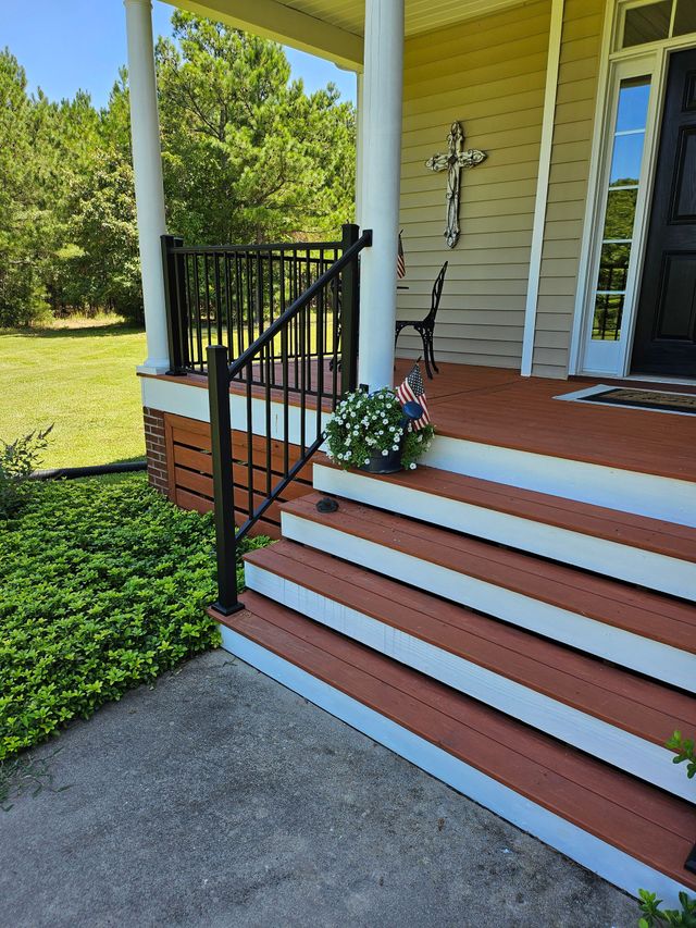 Front porch with red-and-white steps, black railing, white columns, and a potted flower arrangement.