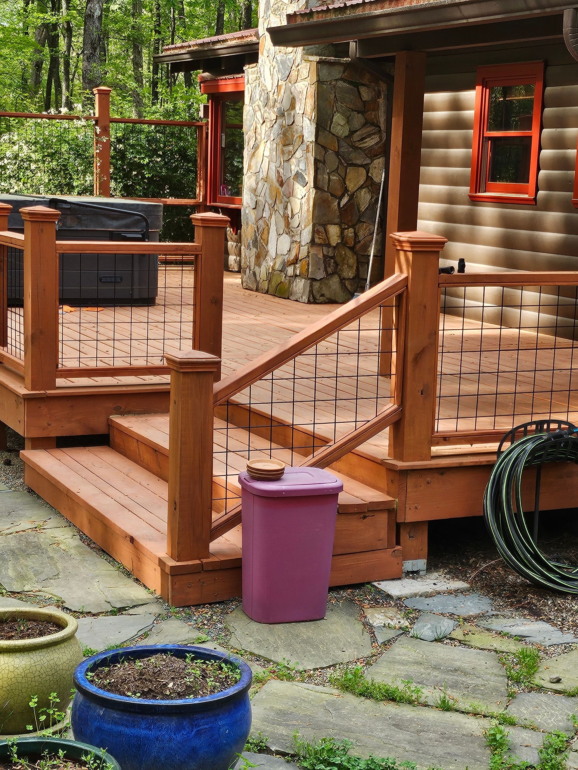 Wooden deck with railings beside a stone house, with potted plants in the foreground.