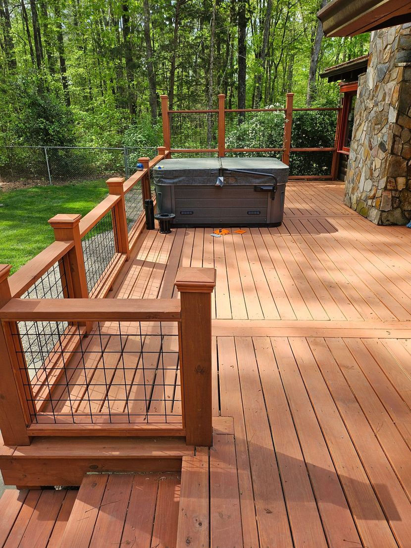Wooden deck with railing, hot tub, and stone wall beside a wooded forest backdrop