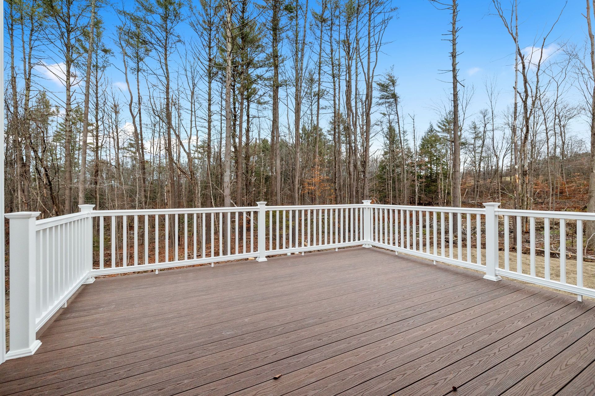 Wooden deck with white railing overlooking a wooded area under a clear blue sky