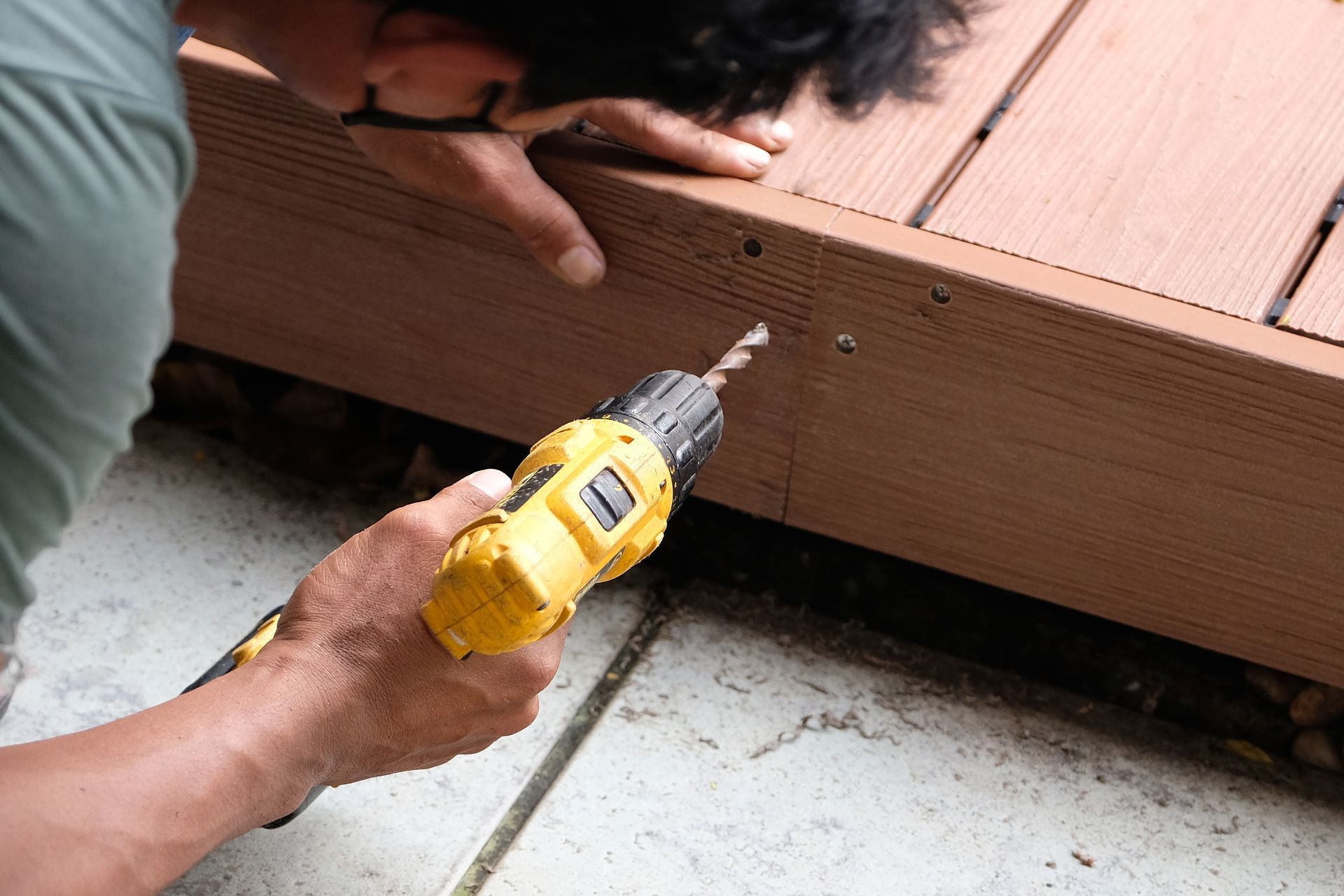 Person drilling a hole into a wooden deck board with a yellow power drill
