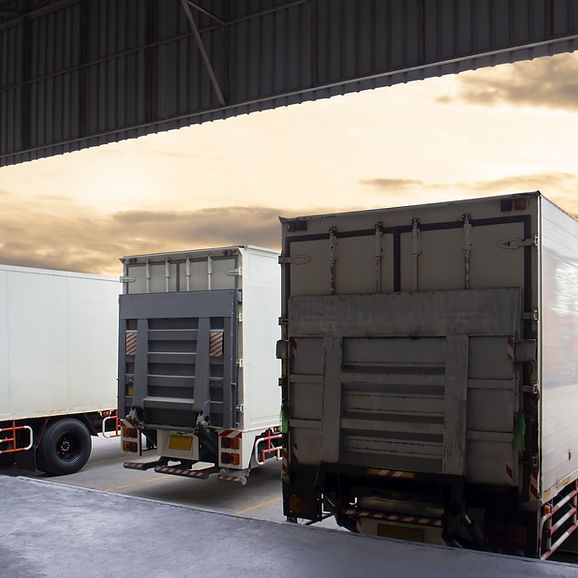 White semi-trucks backed into a loading dock under a warehouse roof.