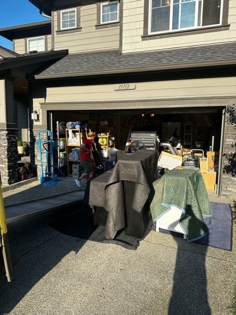 Garage full of packed boxes and furniture being moved. A person is inside the garage, with moving equipment.