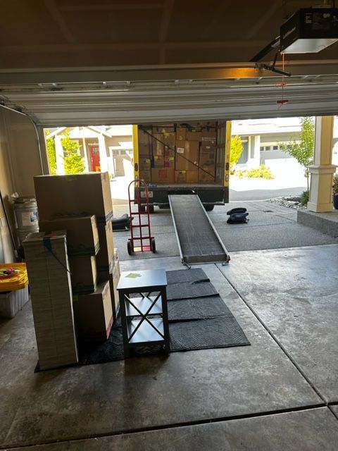 Boxes, ramp, and furniture in a garage, a moving truck is backed up, ready for loading.