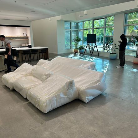 A large white modular sofa in a modern room, two people near. One holding a box, the other looks at phone.