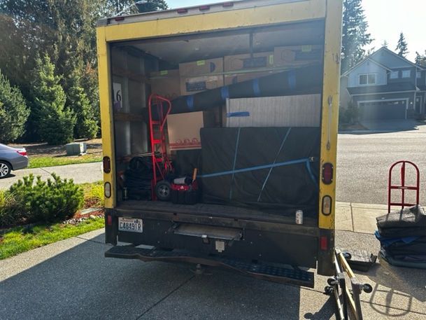 Yellow moving truck loaded with furniture, boxes, and a dolly, parked on a driveway.
