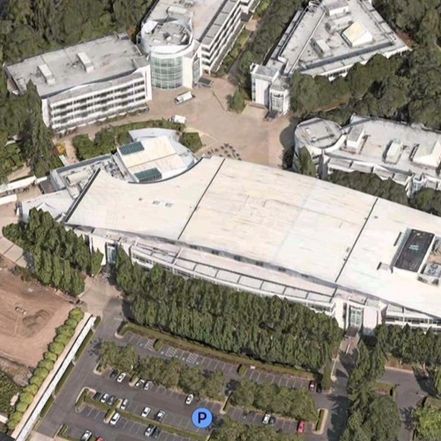 Aerial view of a large modern building complex with parking and surrounding trees.