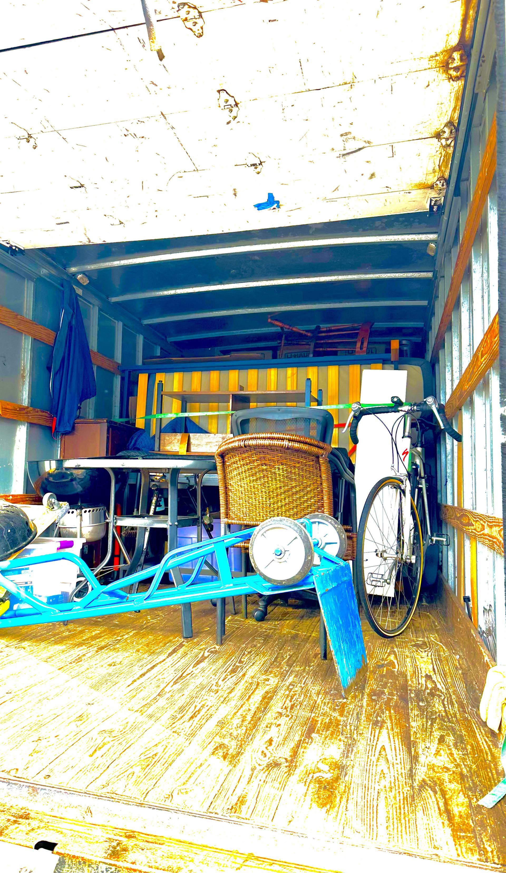 Inside of a truck is filled with items, including a bike, baskets, and a blue object.