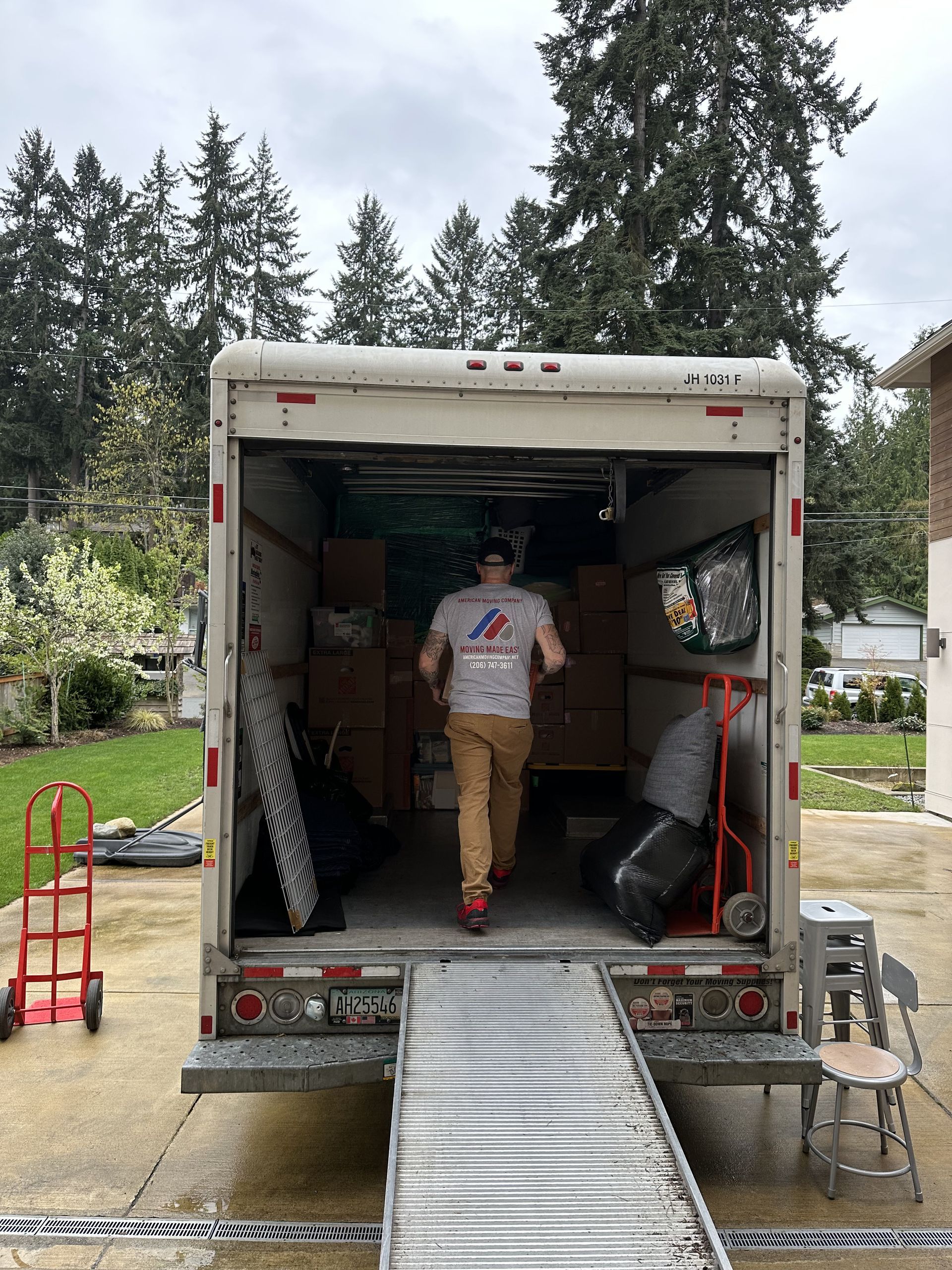 Man walking into an open moving truck, ramp extended, boxes visible inside, overcast day.
