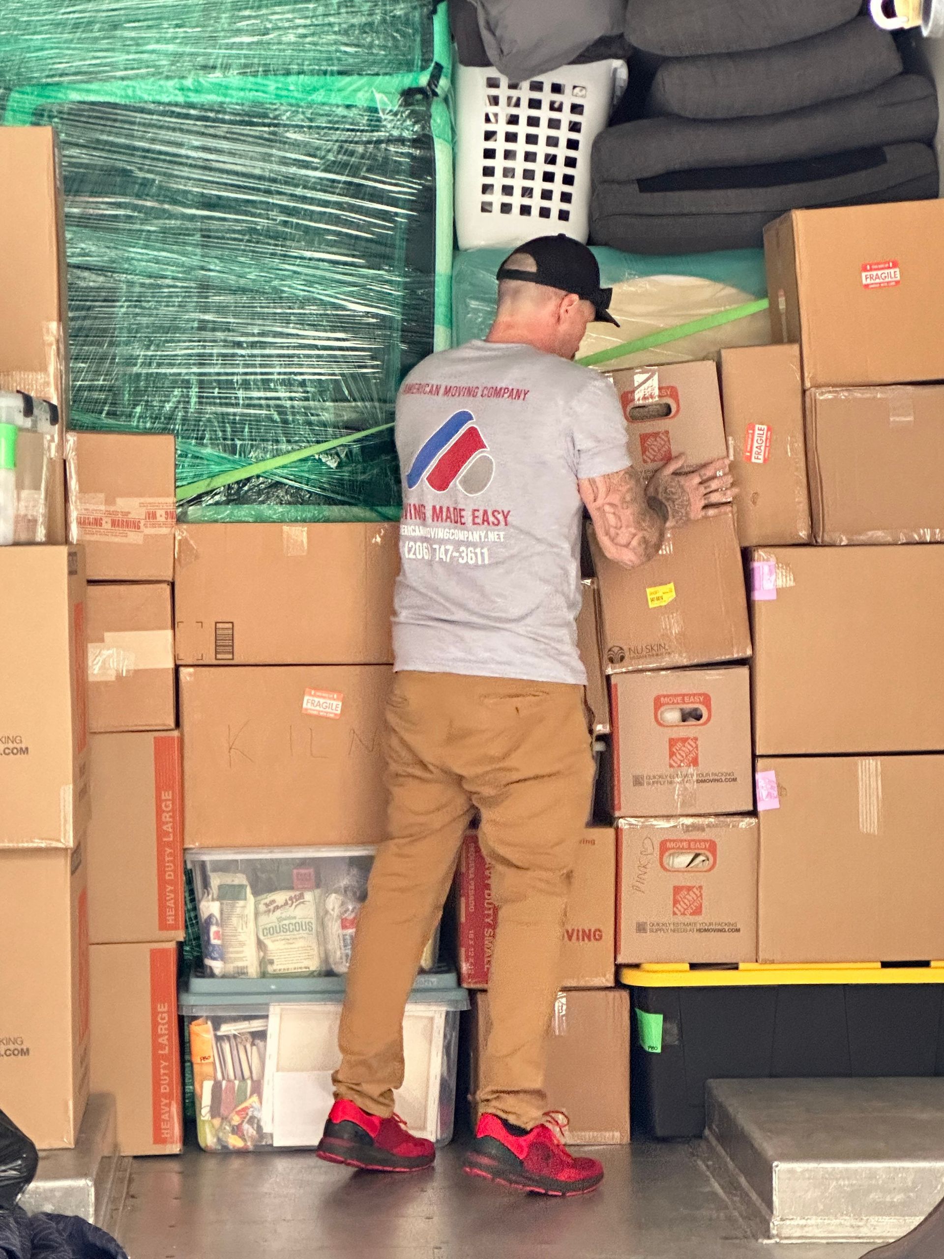 Man in grey shirt and tan pants stacks cardboard boxes in a truck, interior view.