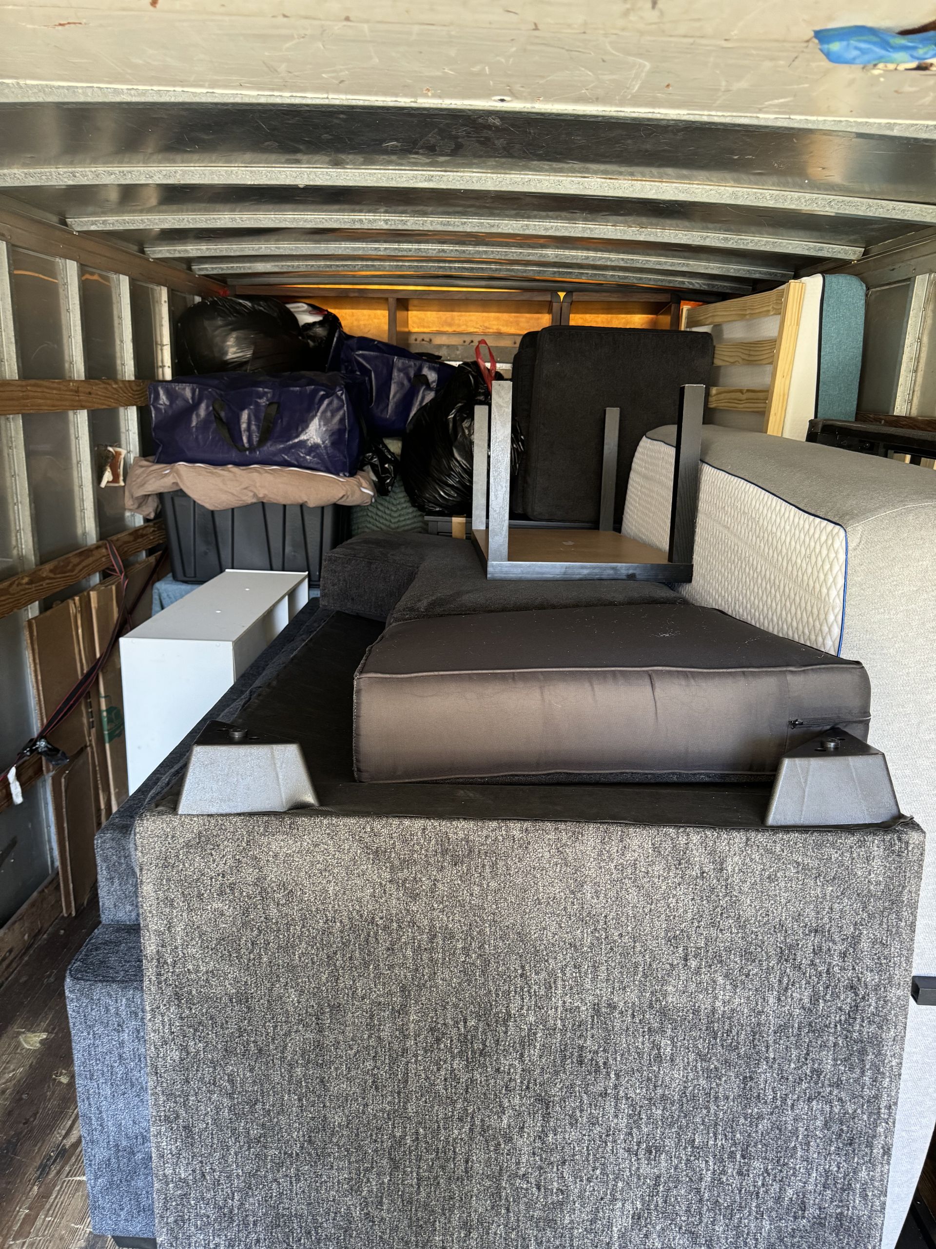Inside a cargo trailer filled with furniture, including a sofa and other large items.