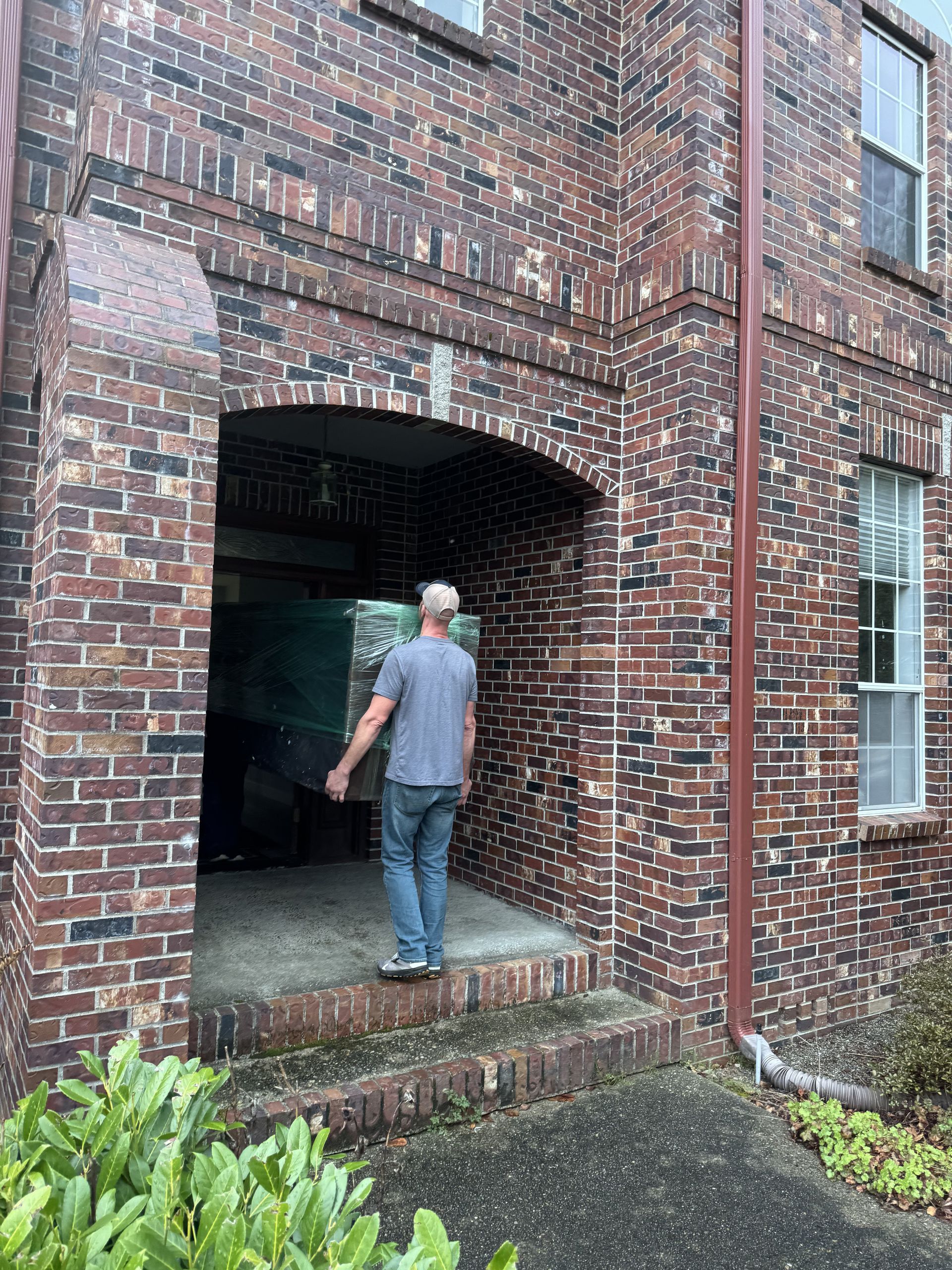 Man carrying a large, wrapped item into a brick building entrance.