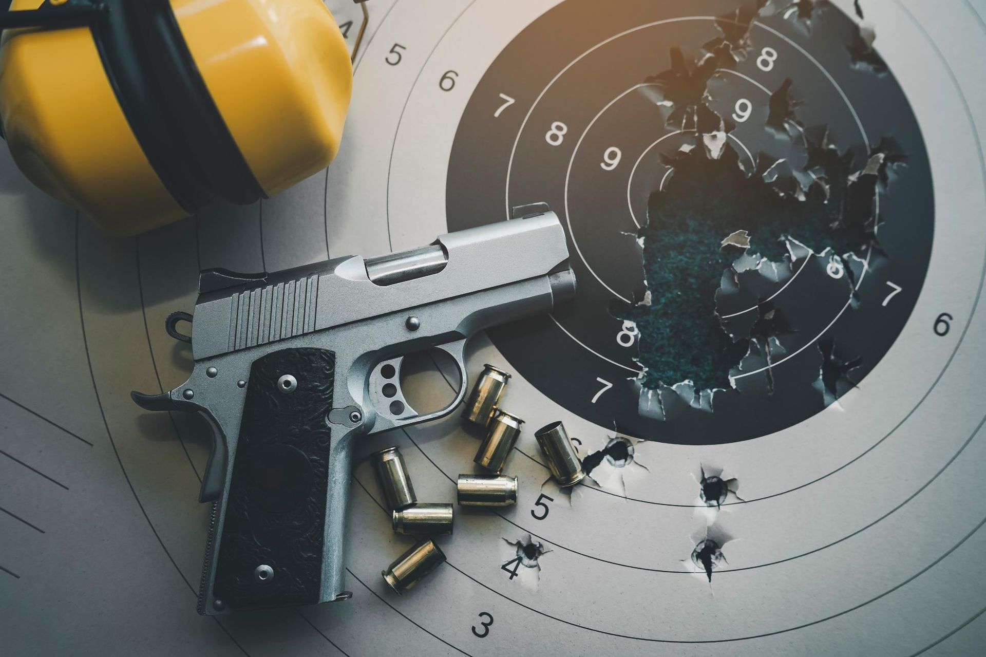 Silver handgun on a target with bullet holes and ammunition; yellow earmuffs in the background.