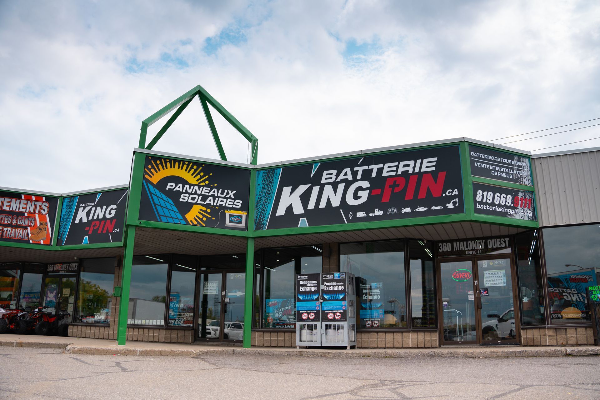 Façade avec des garnitures vertes et une enseigne indiquant « Batterie King-Pin ». Ciel nuageux.