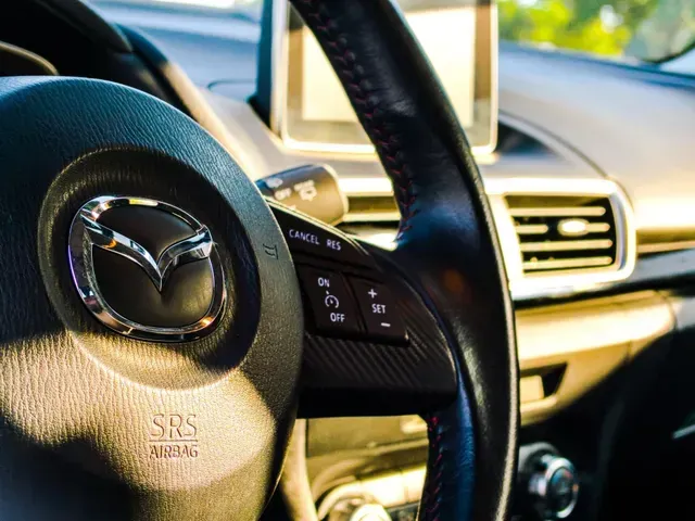 Gros plan sur le volant d'une voiture Mazda, avec le logo et les boutons de commande visibles.