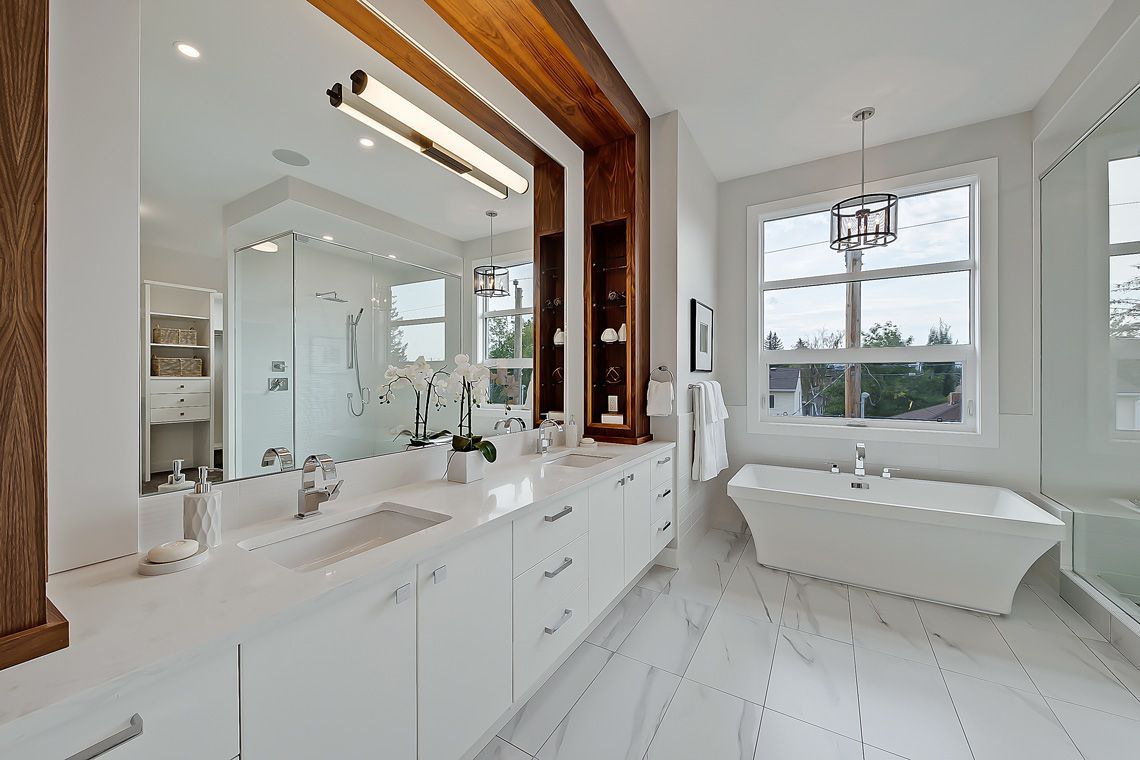 A bright, modern bathroom featuring a white double vanity, large mirror, wooden accents, and a freestanding soaking tub.