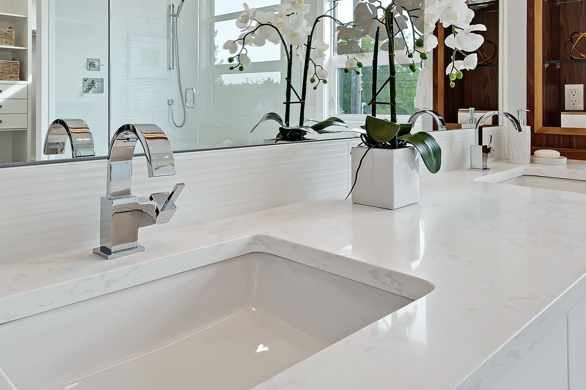 A clean, white bathroom vanity featuring a rectangular under-mount sink, a chrome faucet, and a potted white orchid.