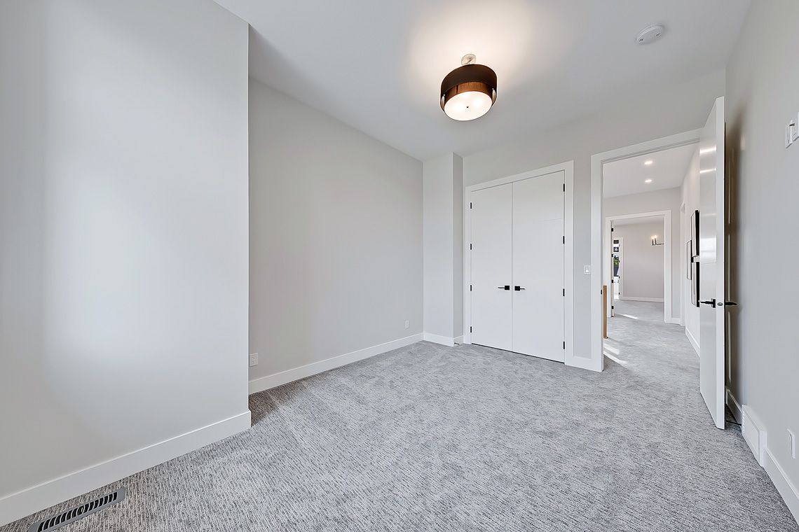 An empty, light-walled bedroom with gray carpet, a white double-door closet, and an open doorway leading to a hallway.