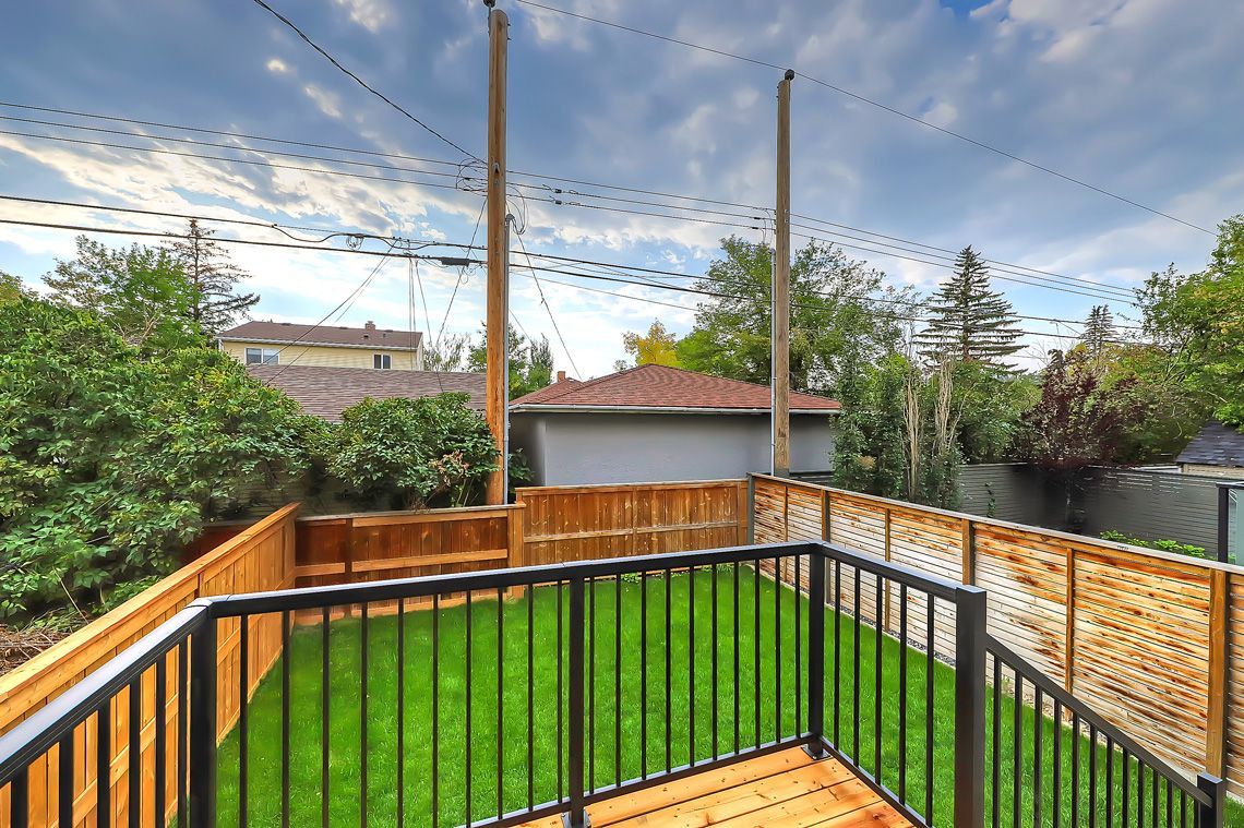A wooden deck with a black metal railing overlooking a green grass backyard enclosed by a wooden fence.