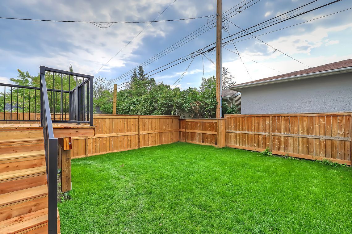 A lush green backyard featuring a wood deck with black railings, a wooden privacy fence, and string lights overhead.