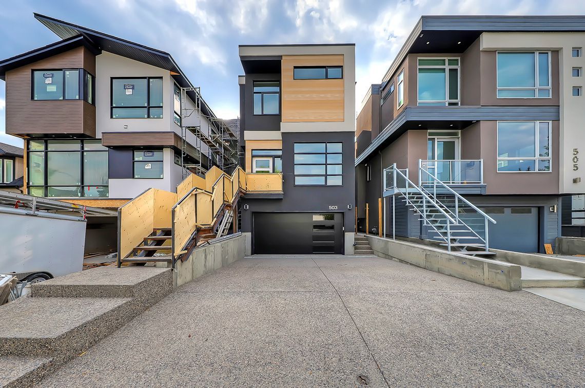 A row of three modern, multi-story houses with contemporary architectural designs and a shared gravel driveway.
