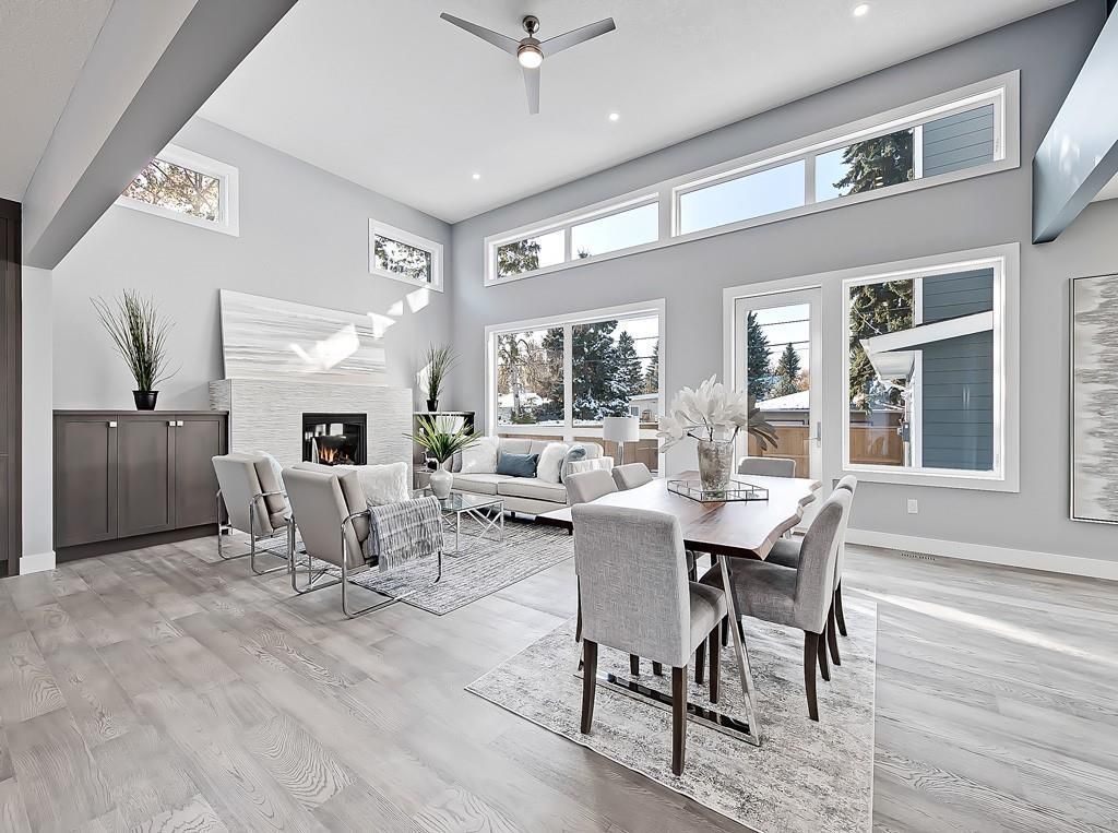 A modern, open-concept living and dining area with light gray walls, light hardwood floors, and large windows.