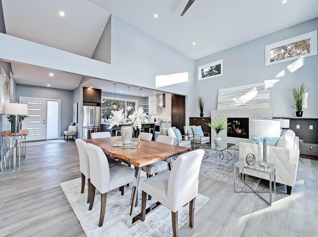 A bright, open-concept living and dining area with a modern stone fireplace, neutral furnishings, and light wood floors.