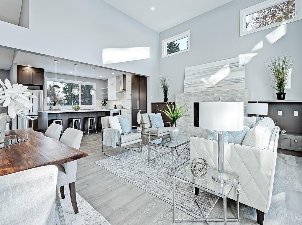 A modern, open-concept living and dining area with white furniture, gray flooring, and a stone fireplace feature wall.