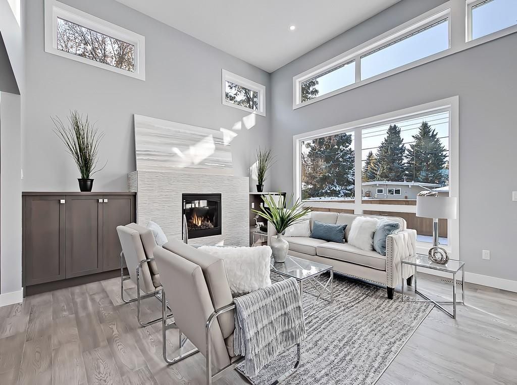 A bright, modern living room with gray walls, two armchairs, a white sofa, a fireplace, and large windows.