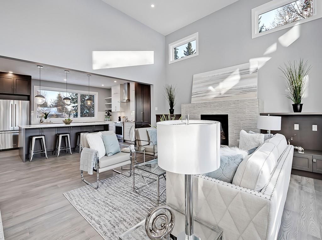 A bright, modern open-plan living room with a white sofa, patterned area rug, fireplace, and kitchen island in the back.