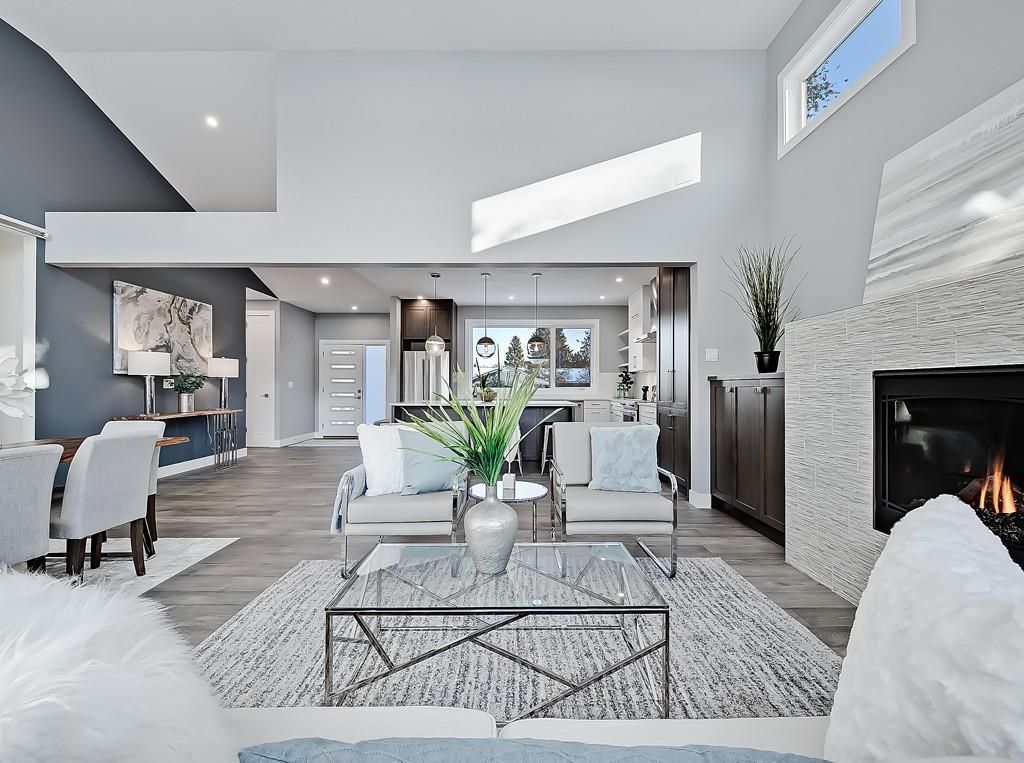 A modern, open-concept living room with a fireplace, glass coffee table, and views into a brightly lit dining area.