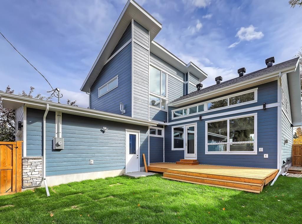 Blue two-story home with a wooden deck in the backyard, set against a bright blue sky with scattered clouds.