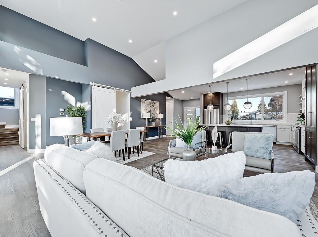 A white couch sits in the foreground of a modern, open-concept living area with grey walls and a bright white kitchen.