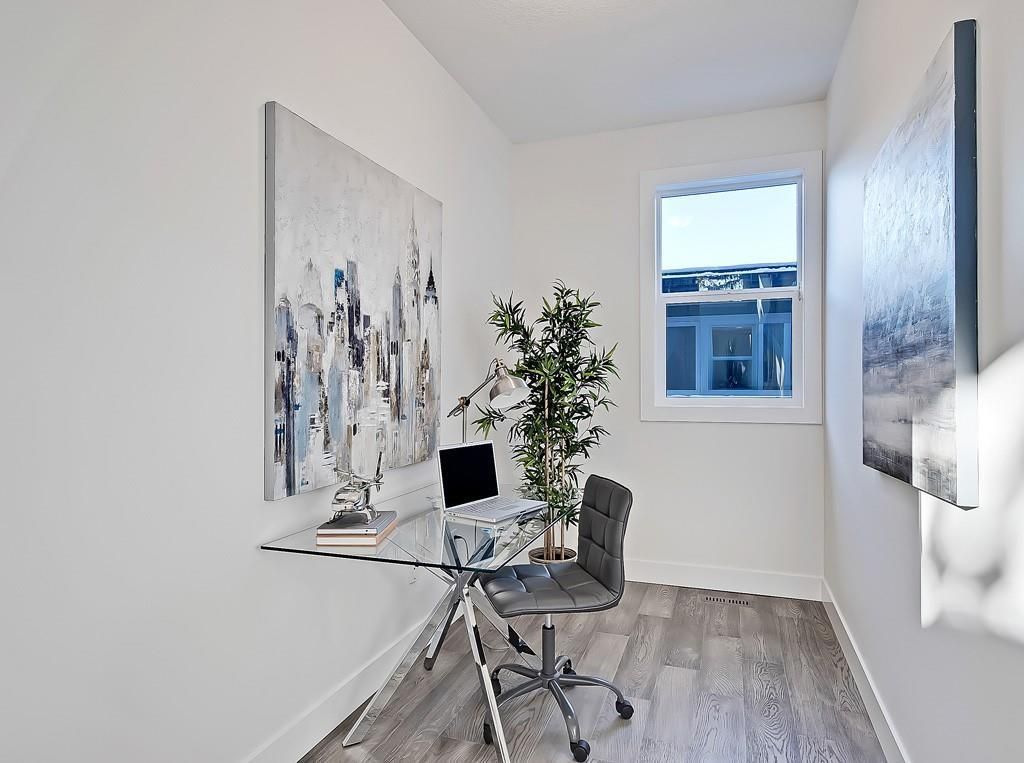 A minimalist home office with a glass desk, grey chair, potted plant, and large abstract art on white walls.