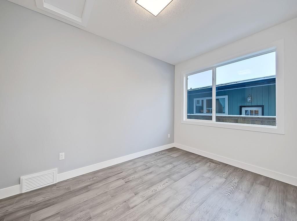 A bright, empty room with light grey walls, white trim, wood-look flooring, and a window looking out at a blue building.