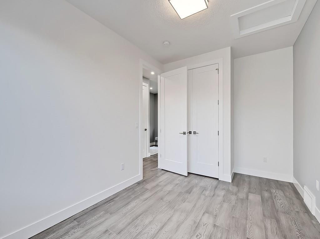 A bright, empty room with light wood-patterned floors, white walls, a flush-mount light, and white closet doors.