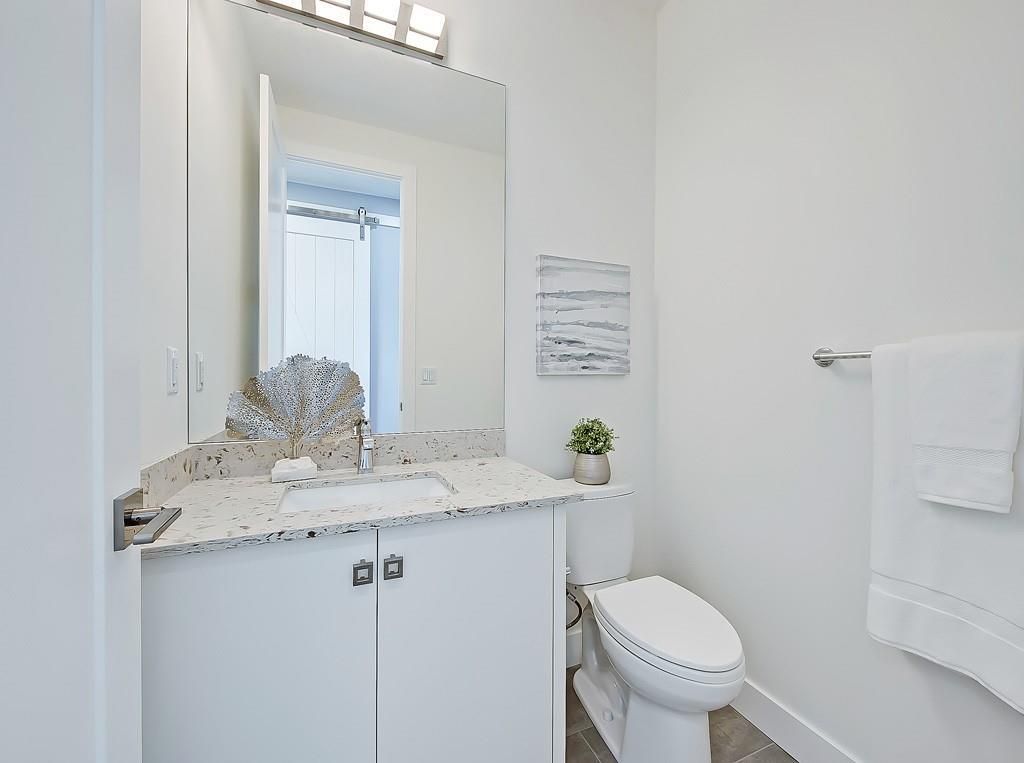 A modern, white-walled bathroom featuring a terrazzo countertop, a sink, a vanity cabinet, a mirror, and a toilet.