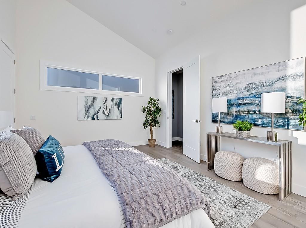 A bright, modern bedroom featuring a bed with textured bedding, a console table with two lamps, and wall art.